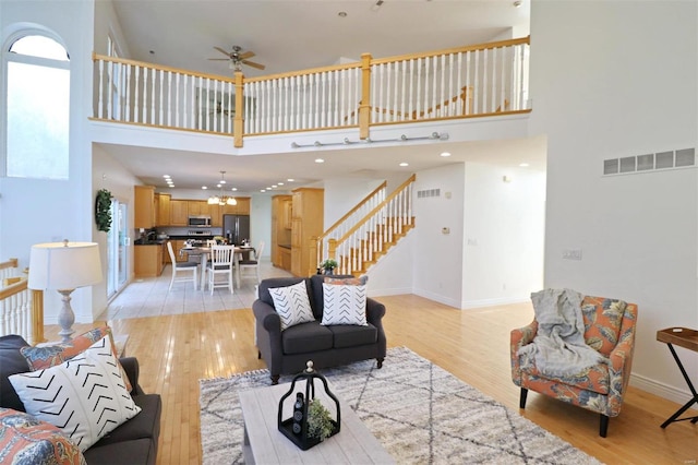 living room featuring light wood-type flooring, a towering ceiling, and ceiling fan