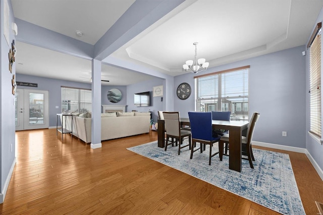 dining area featuring hardwood / wood-style flooring, a notable chandelier, a healthy amount of sunlight, and a raised ceiling