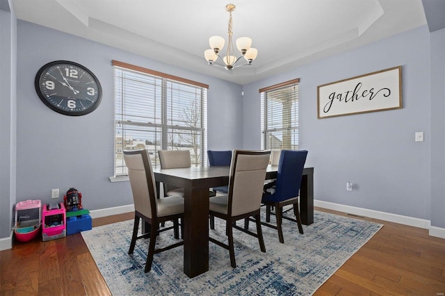 dining room featuring a tray ceiling, a chandelier, and dark wood-type flooring