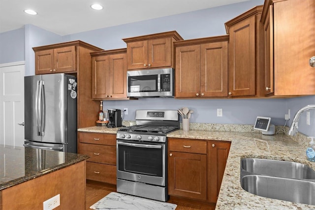 kitchen with light stone countertops, appliances with stainless steel finishes, dark hardwood / wood-style floors, and sink