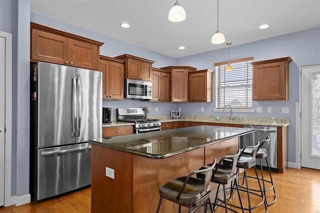 kitchen featuring dark stone counters, hanging light fixtures, light hardwood / wood-style floors, a kitchen island, and stainless steel appliances