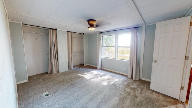 unfurnished bedroom featuring light carpet, ceiling fan, and multiple closets