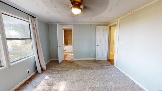 unfurnished bedroom featuring multiple windows, light carpet, ceiling fan, and ensuite bathroom