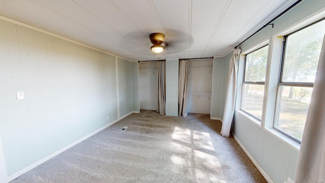 unfurnished bedroom with carpet flooring, ceiling fan, and multiple closets