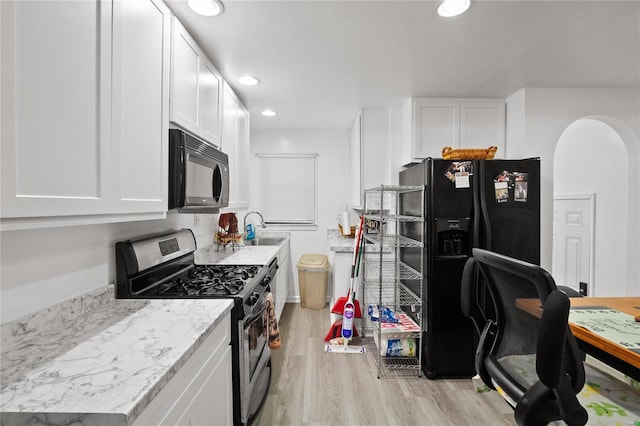 kitchen with black appliances, sink, light stone countertops, light wood-type flooring, and white cabinetry