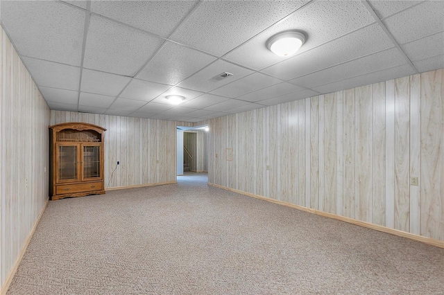 basement with a paneled ceiling, wooden walls, and light colored carpet