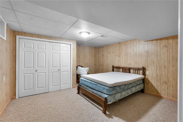 carpeted bedroom featuring a closet, a drop ceiling, and wood walls