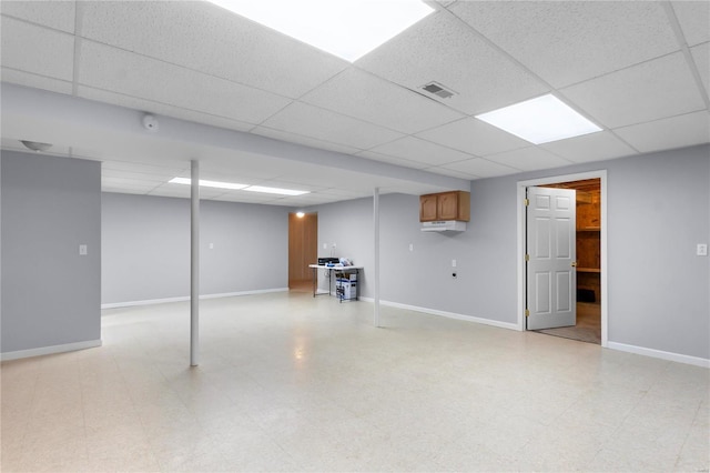 finished basement featuring light floors, visible vents, a drop ceiling, and baseboards