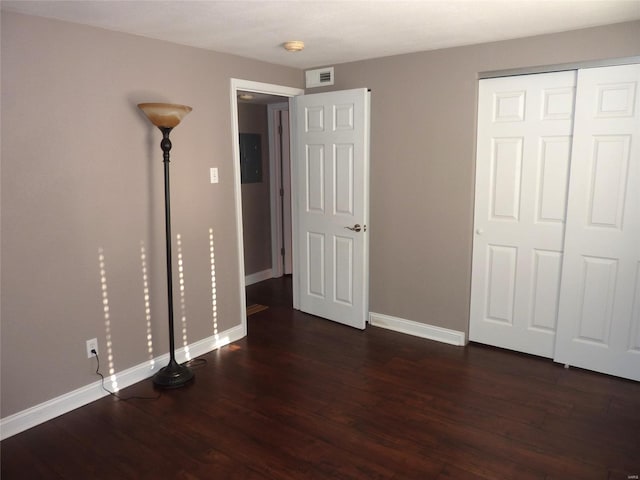 unfurnished bedroom with electric panel, a closet, and dark wood-type flooring