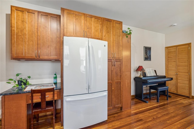 kitchen with white fridge, dark wood-type flooring, and dark stone countertops