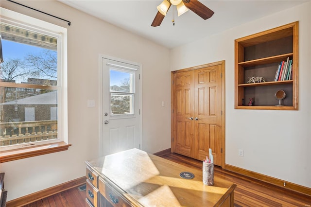 office space featuring ceiling fan, built in shelves, and dark hardwood / wood-style floors