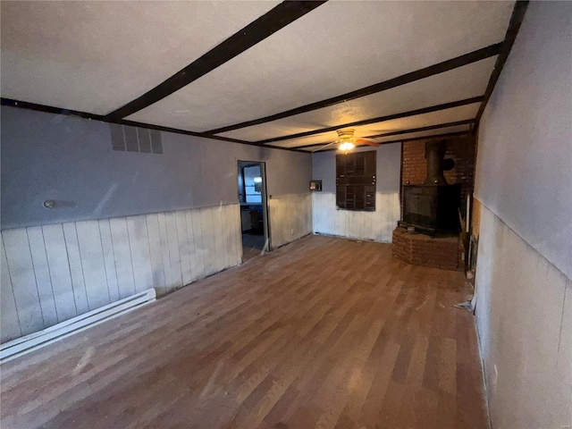 unfurnished living room with beam ceiling, a wood stove, and hardwood / wood-style floors