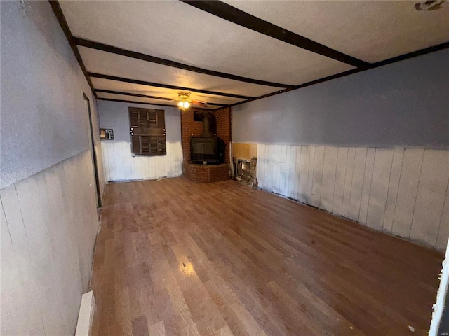 unfurnished living room with beamed ceiling, hardwood / wood-style floors, a wood stove, and wood walls