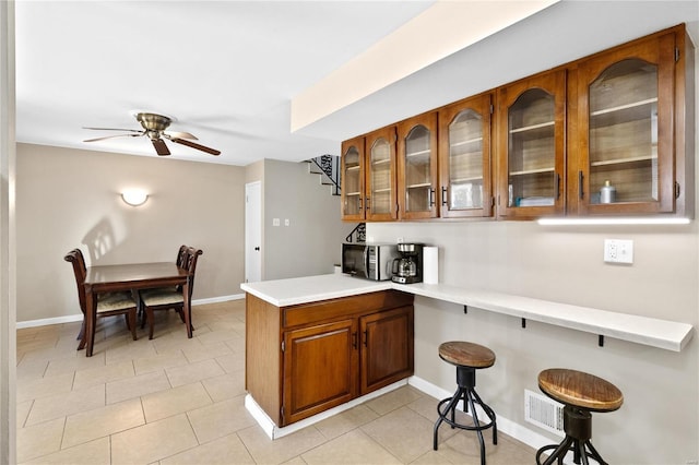 kitchen with ceiling fan, a kitchen bar, kitchen peninsula, and light tile patterned floors