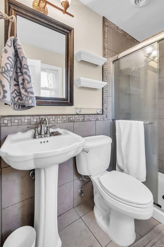 bathroom featuring tile walls, a shower with door, toilet, and tile patterned floors