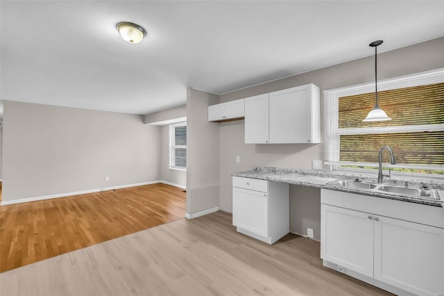 kitchen with white cabinets, sink, light stone countertops, decorative light fixtures, and light hardwood / wood-style floors