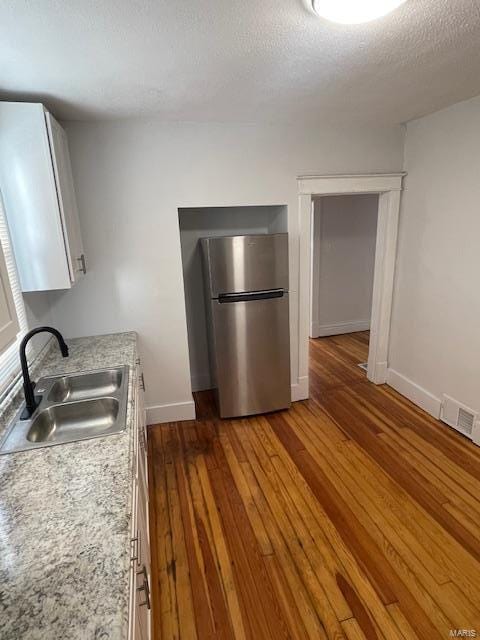 kitchen with stainless steel refrigerator, sink, wood-type flooring, a textured ceiling, and white cabinets