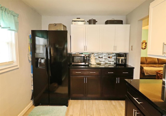 kitchen with backsplash, black refrigerator with ice dispenser, dark stone counters, white cabinets, and light hardwood / wood-style floors