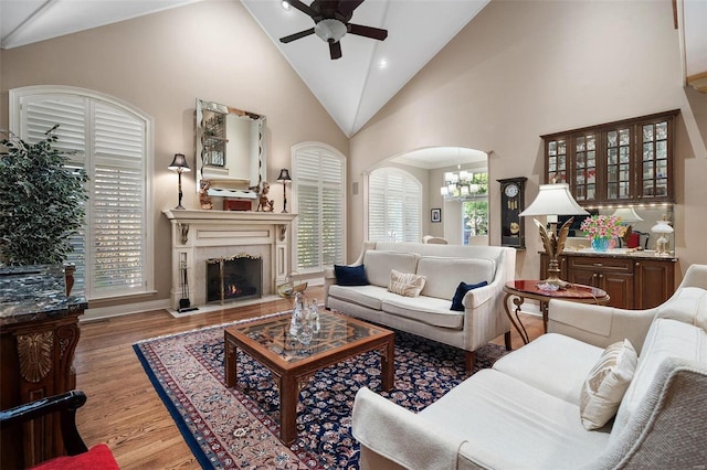 living room with plenty of natural light, high vaulted ceiling, light hardwood / wood-style floors, and ceiling fan with notable chandelier