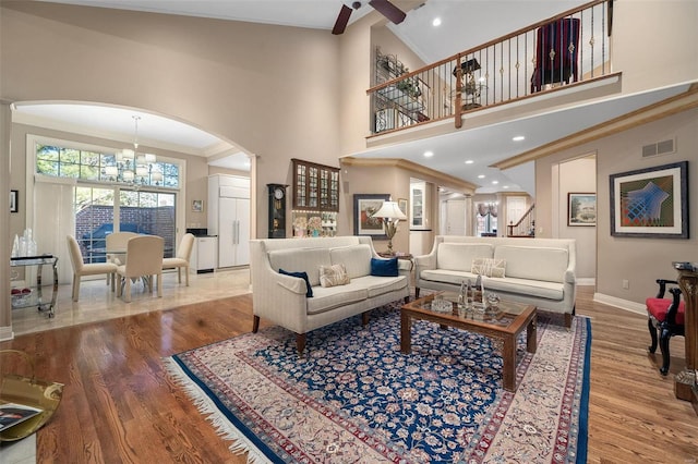 living room featuring hardwood / wood-style floors, ceiling fan with notable chandelier, ornamental molding, and high vaulted ceiling