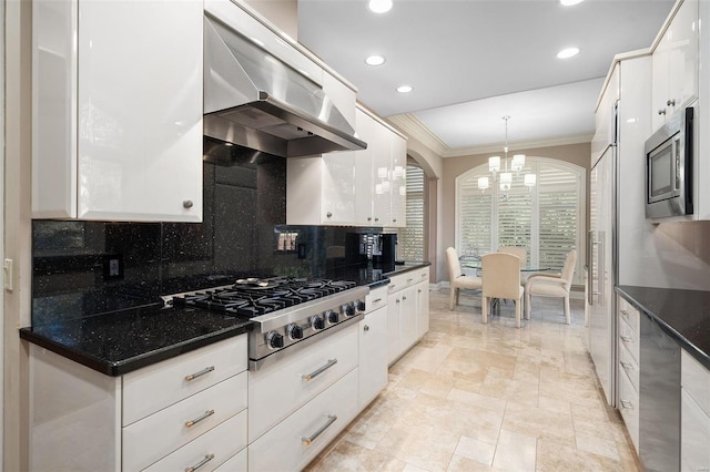 kitchen with appliances with stainless steel finishes, backsplash, wall chimney exhaust hood, decorative light fixtures, and white cabinetry