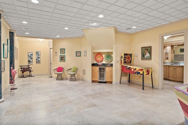 recreation room with a paneled ceiling, beverage cooler, and wet bar