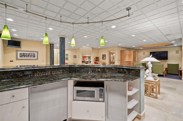 kitchen with stainless steel microwave, white cabinetry, hanging light fixtures, and dark stone counters