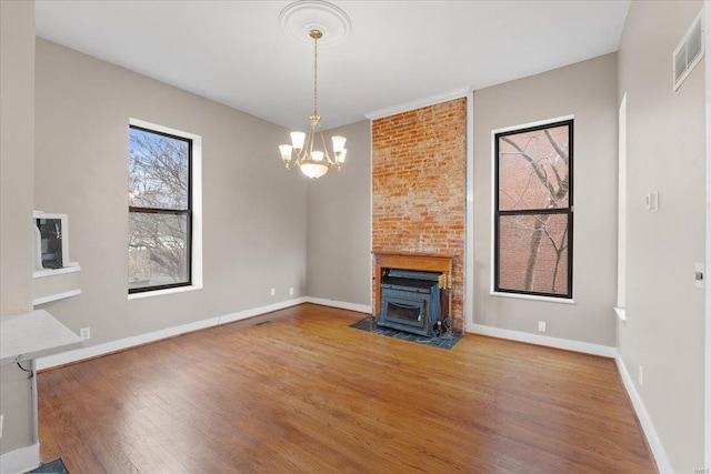 unfurnished living room featuring wood-type flooring, a wood stove, and a notable chandelier