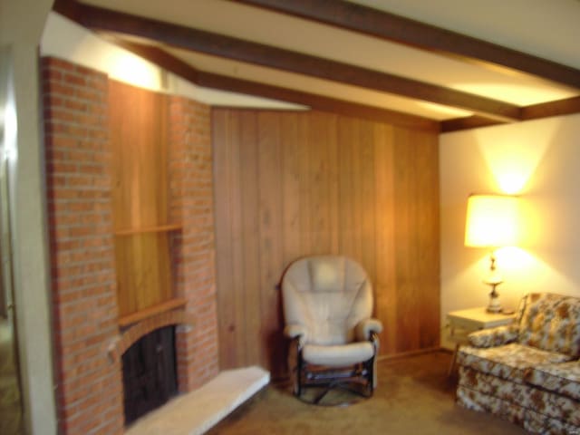 living room with carpet, wooden walls, a fireplace, and beamed ceiling