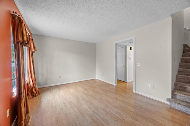 empty room with light wood-type flooring and a textured ceiling