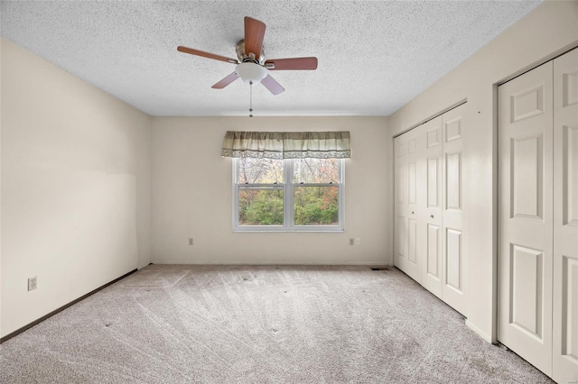 unfurnished bedroom with light carpet, a textured ceiling, two closets, and ceiling fan