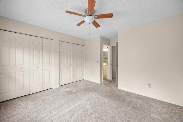 unfurnished bedroom with light carpet, a textured ceiling, two closets, and ceiling fan