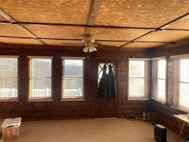 carpeted entrance foyer with wood walls and ceiling fan