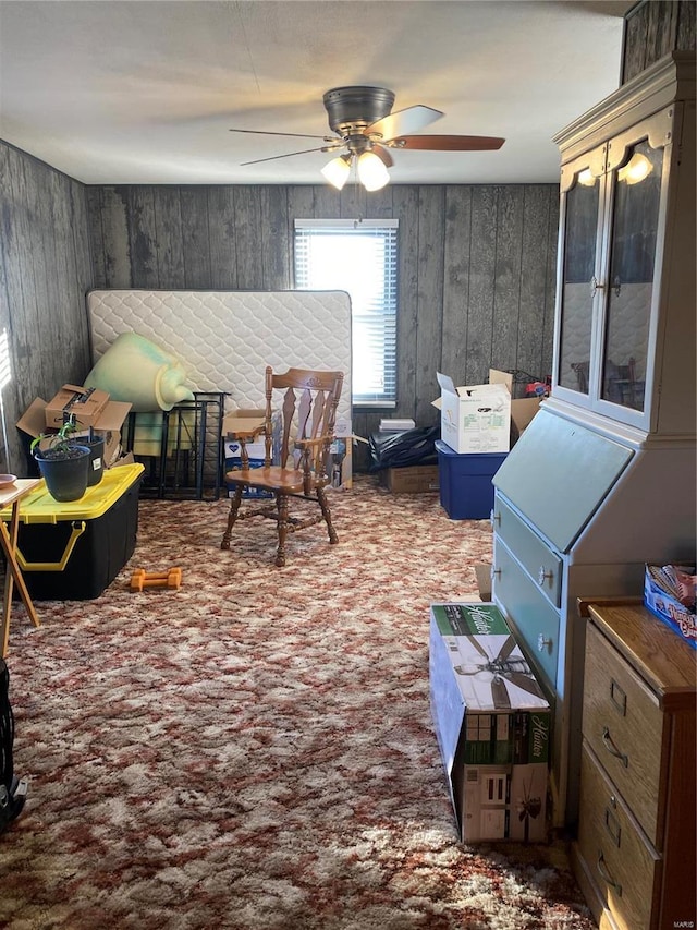 living area featuring carpet flooring, ceiling fan, and wooden walls