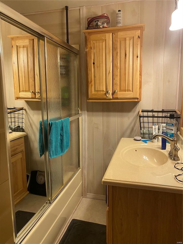 bathroom with wood walls, vanity, and bath / shower combo with glass door