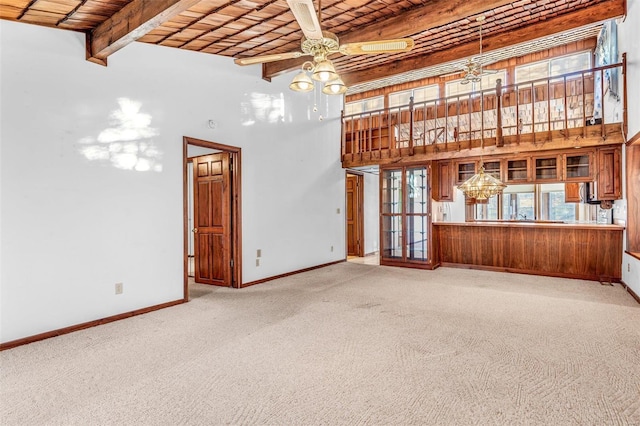 unfurnished living room featuring beam ceiling, wooden ceiling, a towering ceiling, carpet, and ceiling fan with notable chandelier