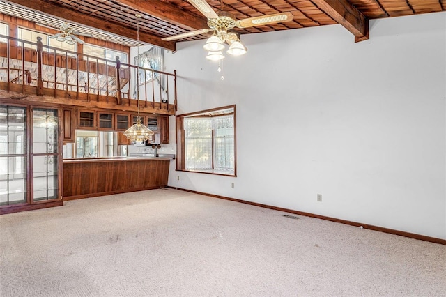 unfurnished living room with carpet flooring, beam ceiling, plenty of natural light, and wooden ceiling