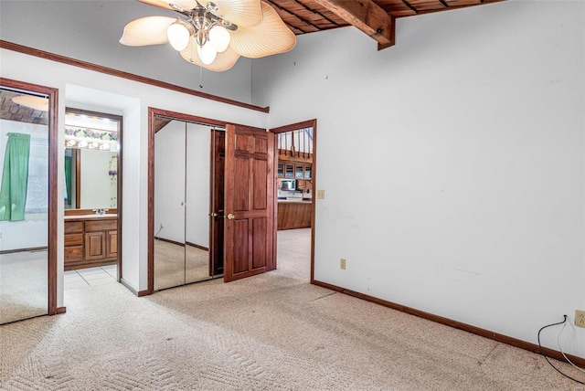 unfurnished bedroom featuring connected bathroom, wood ceiling, light colored carpet, ceiling fan, and vaulted ceiling with beams