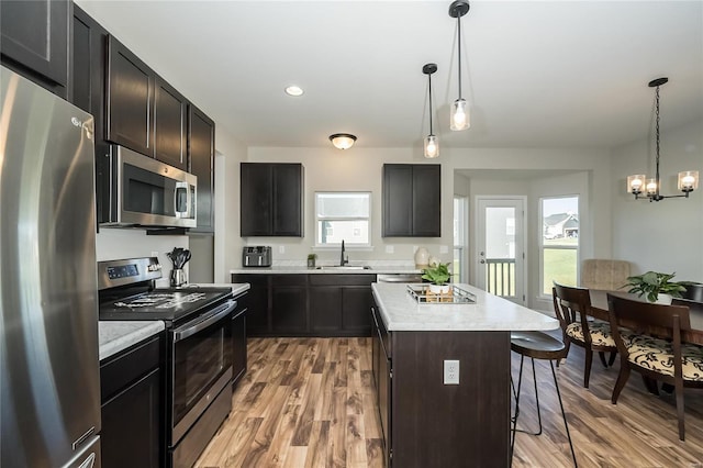 kitchen with sink, light hardwood / wood-style flooring, decorative light fixtures, a kitchen island, and appliances with stainless steel finishes