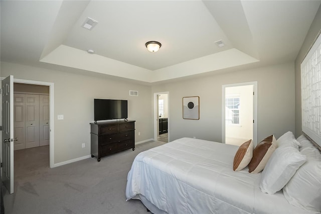 bedroom with a raised ceiling, ensuite bath, and light colored carpet