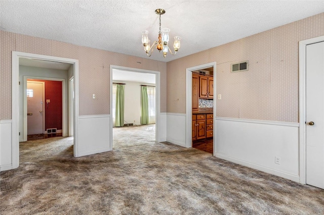 spare room with a textured ceiling, a notable chandelier, and dark colored carpet