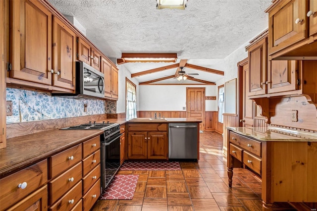 kitchen with lofted ceiling with beams, wooden walls, ceiling fan, a textured ceiling, and stainless steel appliances