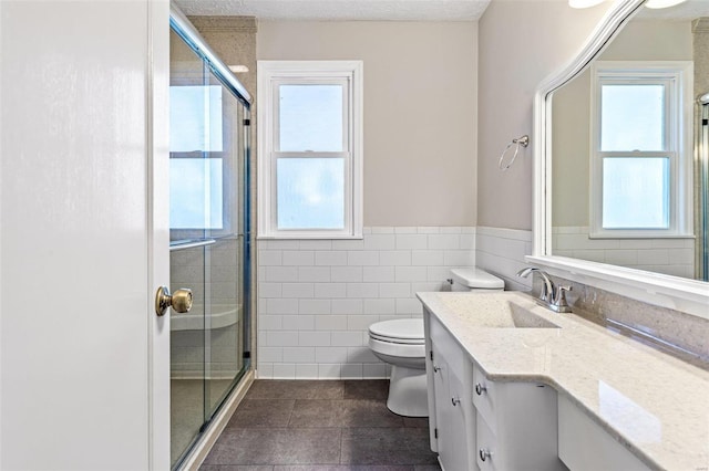 bathroom with toilet, tile patterned floors, tile walls, and a healthy amount of sunlight