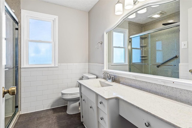 bathroom with vanity, a shower with door, tile patterned floors, toilet, and tile walls