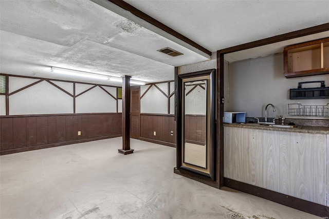 basement with sink, a textured ceiling, and wooden walls