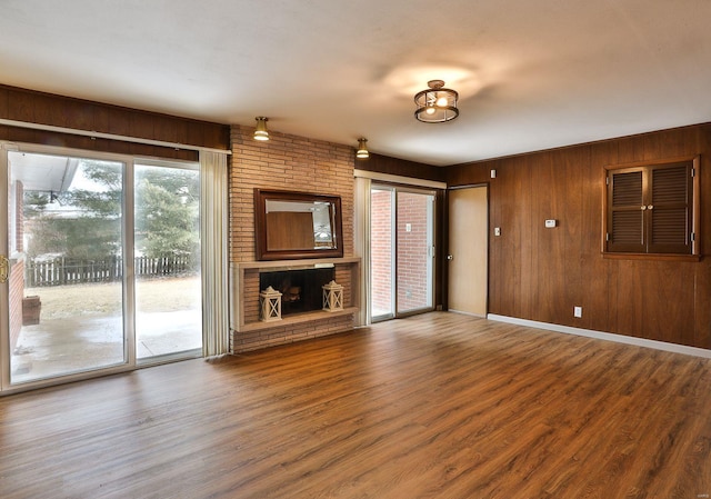 unfurnished living room featuring a brick fireplace, wooden walls, and wood-type flooring