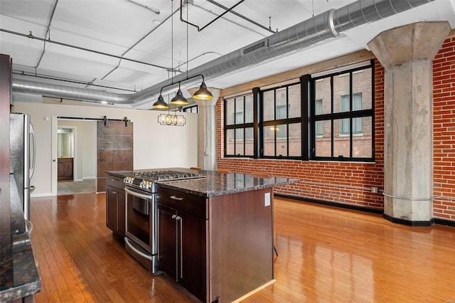 kitchen featuring dark stone counters, brick wall, stainless steel appliances, pendant lighting, and a barn door