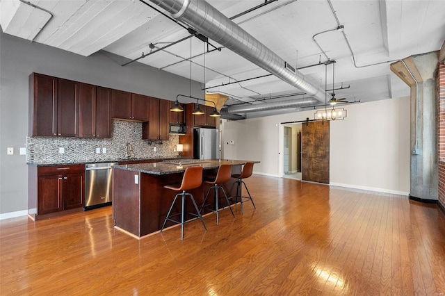 kitchen with a breakfast bar, a barn door, light wood-type flooring, a kitchen island, and stainless steel appliances