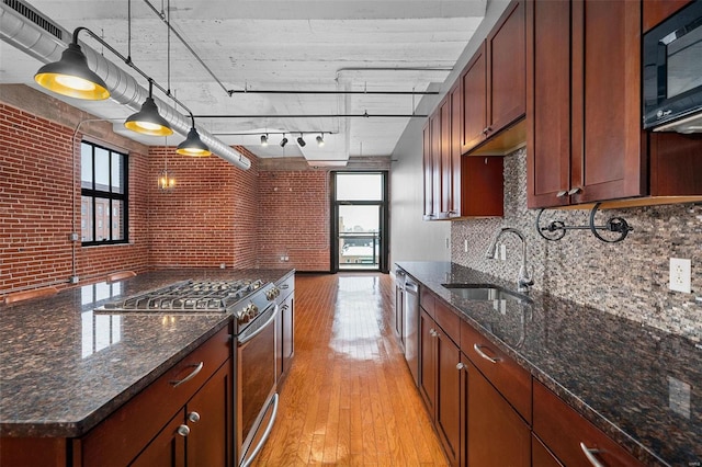 kitchen featuring appliances with stainless steel finishes, brick wall, sink, light hardwood / wood-style floors, and hanging light fixtures