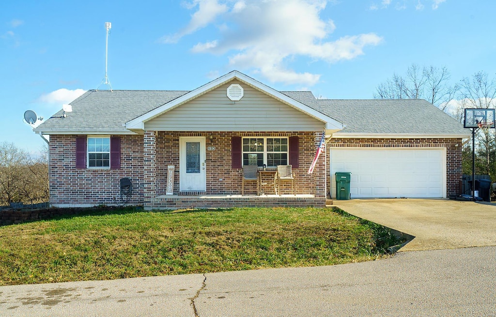 single story home with driveway, a garage, covered porch, a front lawn, and brick siding